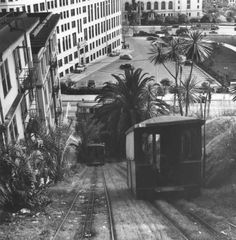 an old black and white photo of a train going down the tracks in front of buildings