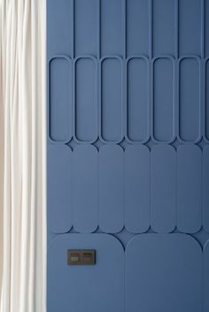 a blue wall with white curtains and a black door handle on the left hand side