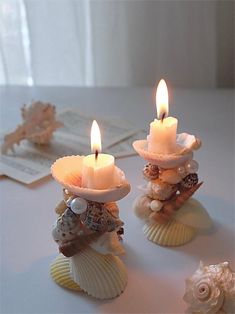 two candles are sitting on shells with seashells