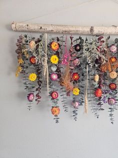 a bunch of flowers are hanging from a wooden stick on the wall next to a white wall