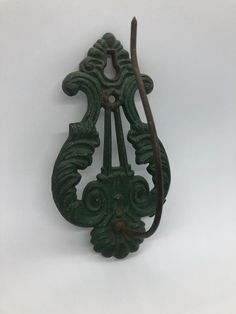 an old green metal hook with ornate designs on it's side, hanging from a white wall