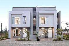 two story houses with white doors and windows in front of each other on a brick driveway