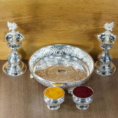 three silver candlesticks and two bowls with different colored liquids in them on a table