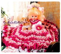 a doll sitting on top of a pink and white crocheted blanket next to a teddy bear