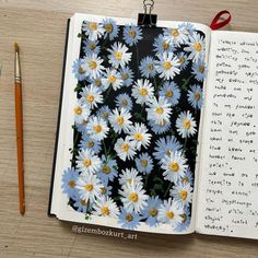 an open notebook with daisies on it next to a pair of scissors and pencils