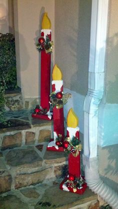 three red candles with christmas decorations on them sitting in front of a stone wall and steps