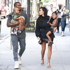 the couple are walking down the street with their daughter, who is holding an infant