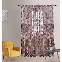 a living room with a yellow chair and window covered in pink flowers on the curtains