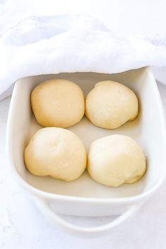 four uncooked doughnuts in a white dish on a table with a towel