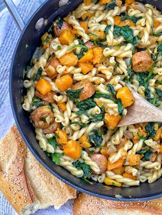 a skillet filled with pasta and vegetables on top of a blue towel next to bread