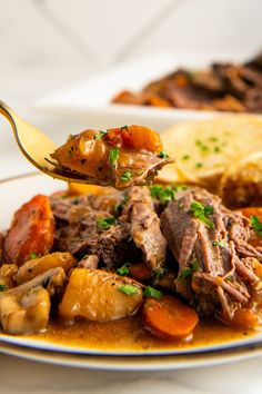 a spoonful of stew with potatoes and carrots on a white plate next to bread