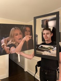 the man is holding up two pictures in front of his face and pointing to them