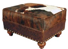 a brown and white cowhide ottoman with studded wooden legs on an isolated white background