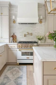 a white and gold kitchen with an oven, stove, sink, and rug on the floor