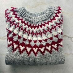 "A warm, chunky-knit pullover style sweater with a lovely geometric pattern around the yoke. It's a soft grey with white and burgundy/red. This sweater was worked bottom-up in the round to the underarm, the sleeves were worked separately, and then all parts were joined together on one needle to the yoke and neck opening. Likely a large, but please see details below. The measurements are taken while the sweater is laying flat. Measures:  20\" (51 cm) across shoulders (roughly, as the shoulders slope)  26\" (66 cm) across chest 31\" (78.75 cm) from front neck to hem 18\" (45.75 cm) from underarm to end of sleeve 52\" (132 cm) around at bottom hem" Nordic Style Chunky Knit Sweater, Nordic Chunky Knit Sweater, Gray Nordic Sweater For Fall, White Scandinavian Sweater For Fall, White Scandinavian Style Sweater For Fall, White Scandinavian Style Fall Sweater, Cozy Gray Chunky Knit Pattern, Cozy Fair Isle Pattern Sweater, Scandinavian Sweater With Fair Isle Pattern For Cold Weather