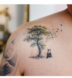 a man with a tree tattoo on his shoulder and chest, sitting under a tree