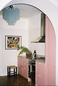 a kitchen with pink cabinets and an arched doorway leading to the dining room, which also has a painting on the wall