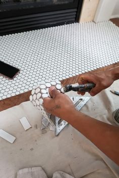 a man is working on a tile floor in his living room with a fireplace and cell phone