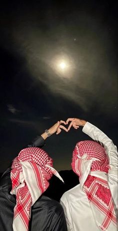 two people wearing headscarves making the shape of a heart with their hands in the air