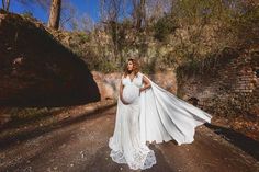 a pregnant woman wearing a white gown and cape standing in the middle of a road