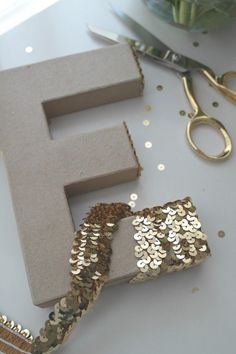 the letter f is made out of gold sequins and sits next to scissors