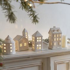 some small white houses are sitting on a mantle next to a candle and christmas tree