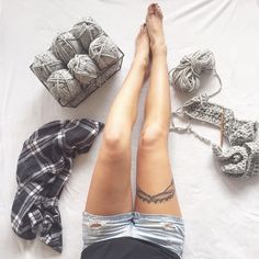 a woman laying on top of a bed with her legs crossed next to some balls of yarn