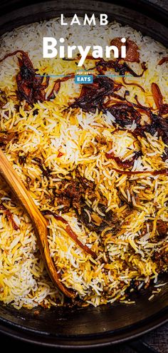 a pan filled with rice and meat next to a wooden spoon