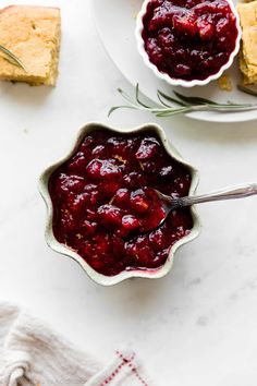 a bowl of cranberry sauce next to two plates with slices of bread on them