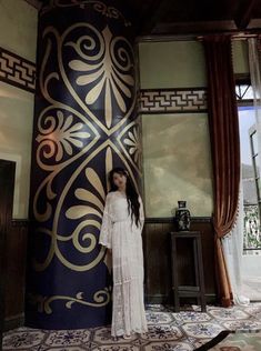 a woman standing in front of a tall blue and gold column next to a window