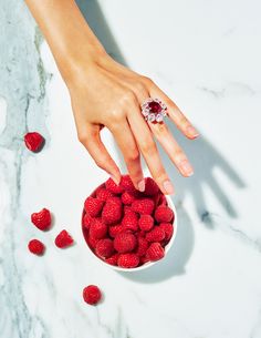 a woman's hand reaching for raspberries in a bowl on a marble surface