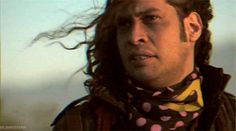 a man with long hair wearing a polka dot scarf and looking off to the side