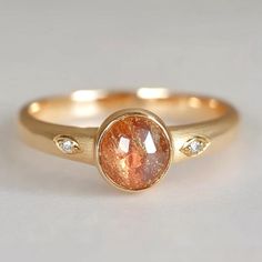 a gold ring with an orange and white diamond in the center, sitting on a table