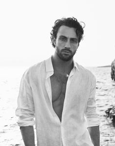 a man standing in front of the ocean wearing a white shirt and no shirt on