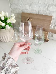 a person holding a wine glass in front of two empty wine glasses on a counter