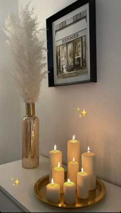 some lit candles are on a tray in front of a framed picture and a vase