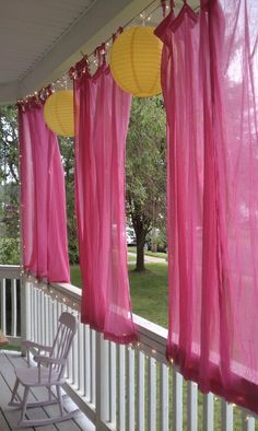 pink curtains are hanging on the front porch with white railings and chairs under them