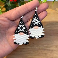 a pair of black and white gnome earrings on top of a wooden table next to a potted plant