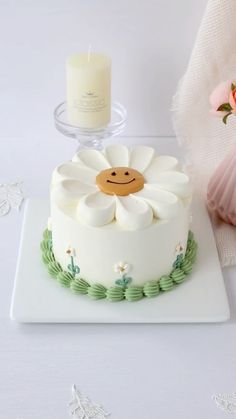 a white cake sitting on top of a table next to a vase with flowers and a candle