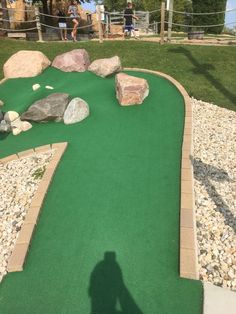 a miniature golf course with rocks and grass in the foreground, people standing on the other side