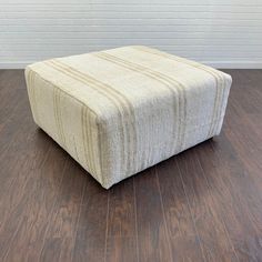 a square footstool sitting on top of a hard wood floor next to a brick wall