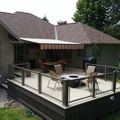 a deck with chairs and an umbrella on it in front of a house that has a grill