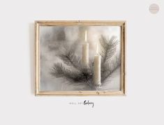 two candles are sitting in front of a framed photograph with pine needles and snow on it