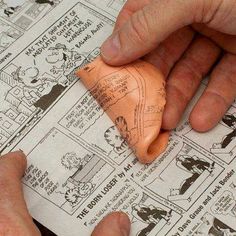 two hands are holding an object on top of a newspaper with cartoon drawings in it