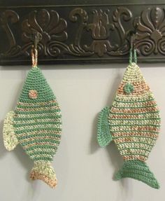 two crocheted fish hanging from hooks on a wall in front of a mirror