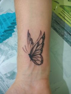 a small butterfly tattoo on the wrist is shown in black and grey ink, with white wings