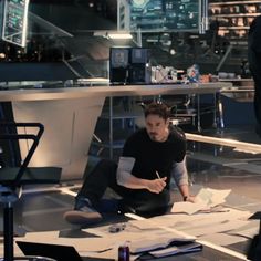 a man sitting on the floor in front of a desk with papers and pens next to him