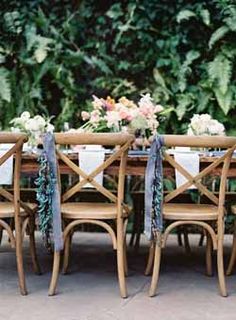 an outdoor table with chairs and place cards on it, surrounded by greenery in the background