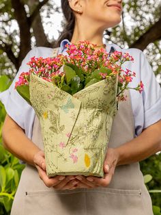 a woman holding a potted plant with pink flowers in it's hands and smiling