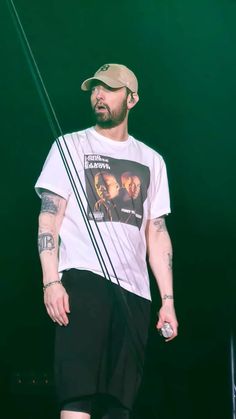 a man standing on stage wearing a hat and t - shirt with the band's logo